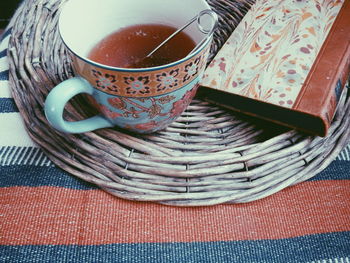 High angle view of strainer in black tea by book on wicker