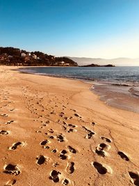 Footprints on sand at beach against clear blue sky