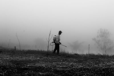 Man spraying pesticides on field against sky