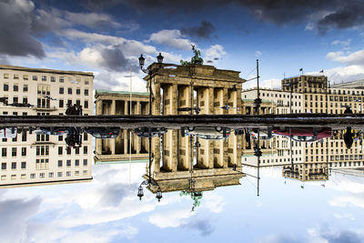 Reflection of brandenburg gate in canal against cloudy sky