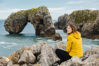 Woman sitting on rock by sea against sky