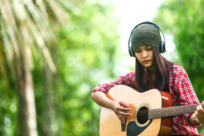 Young woman playing acoustic guitar while sitting at park