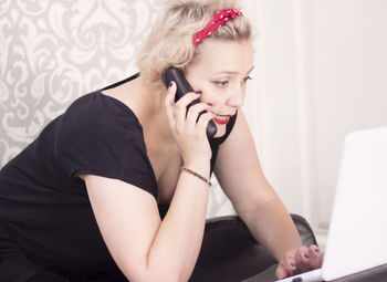 Female hairdresser talking on cordless phone while using laptop in salon