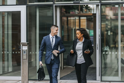 Male and female business colleagues talking while leaving from office building