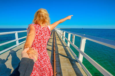 Cropped image of boyfriend holding girlfriend hand on pier by sea