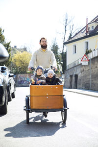 Happy father with two children riding cargo bike in the city