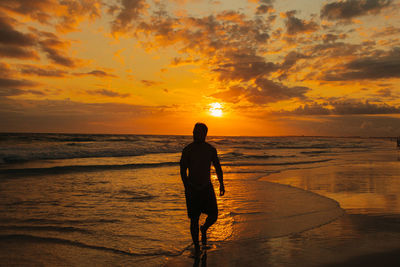 Silhouette woman walking at beach against sky during sunset