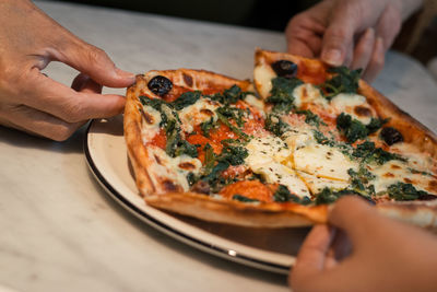 Close-up of hands holding pizza slices on table