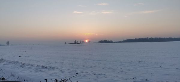 Scenic view of snow covered field against sky during sunset