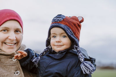 Portrait of cheerful mother with toddler daughter against sky during winter