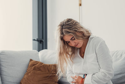 Side view of young woman sitting on bed at home