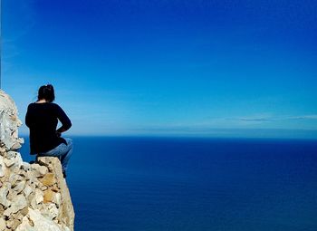 Rear view of woman sitting on rock against sea