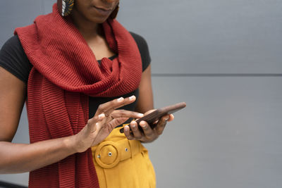 Woman wearing scarf using smart phone in front of gray wall