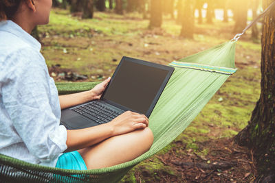 Midsection of woman using laptop while sitting on hammock