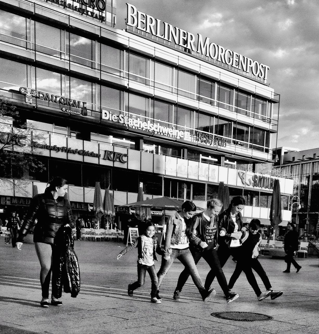 architecture, building exterior, men, large group of people, built structure, person, lifestyles, city, walking, city life, street, leisure activity, text, sky, full length, casual clothing, mixed age range, shopping, day