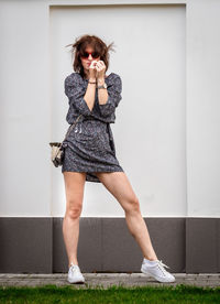 Full length portrait of young woman standing against wall