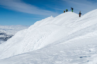 People climbing on snowcapped mountain against sky