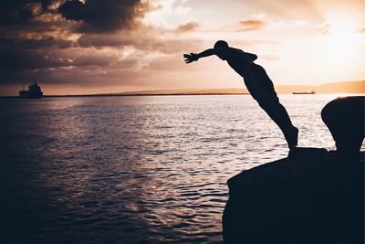 Silhouette man jumping in sea against sky during sunset