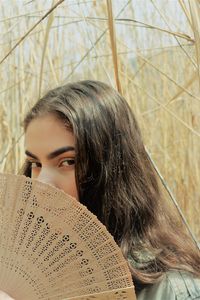 Close-up portrait of young woman in field  holding fan