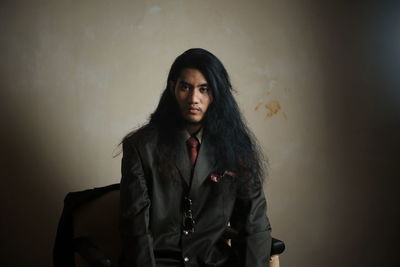 Portrait of man with long hair wearing suit against wall