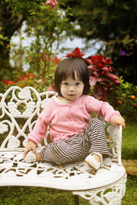 Portrait of cute girl sitting on bench in park