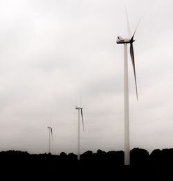 Low angle view of windmills on silhouette field against sky