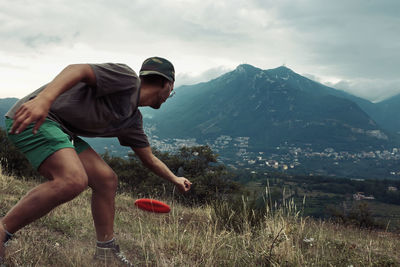 Man throwing plastic disc on field against mountain