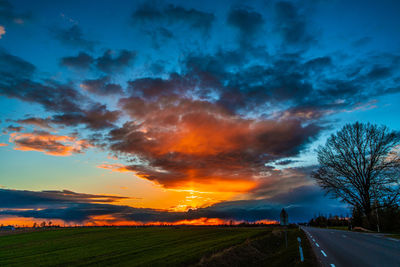 Road amidst field against sky during sunset