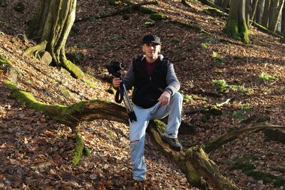 Portrait of man with tripod and camera in forest