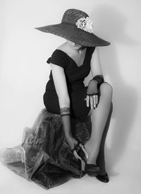 Midsection of woman wearing hat sitting against white background