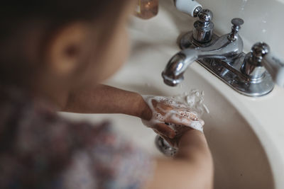 High angle of preschool aged girl washing hands in sink with soap