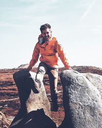 Young man standing on rock against sky