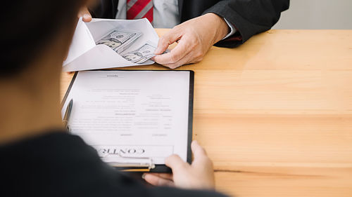 Midsection of man holding paper while sitting on table