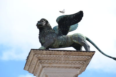 Low angle view of birds on statue against sky