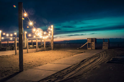 Illuminated street lights on road against sky at night