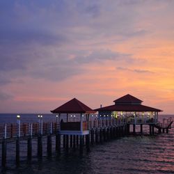 Stilt house on beach against sky during sunset