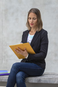 Woman sitting on clipboard against wall