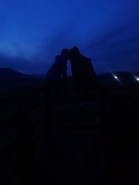 Silhouette people on mountain against blue sky