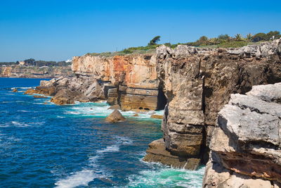 Rock formations by sea against clear blue sky