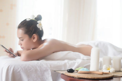 Young woman using phone while lying on massage table in spa