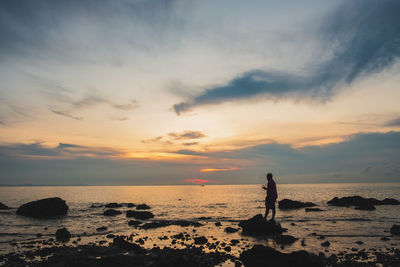 Silhouette rocks on beach against sky during sunset