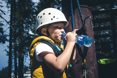 Small boy drinking water while taking a break on treetop during canopy tour in nature.