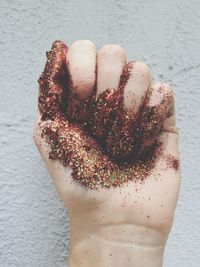 Cropped hand with glitters against wall