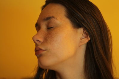 Close-up portrait of young woman against orange background