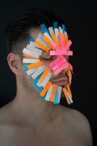 Close-up of shirtless man with adhesive notes on face against black background