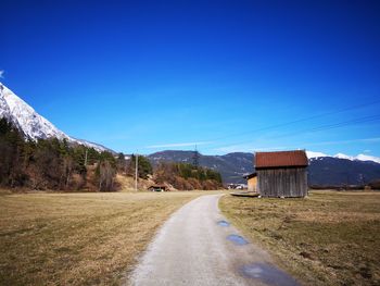 Empty road amidst field against clear blue sky