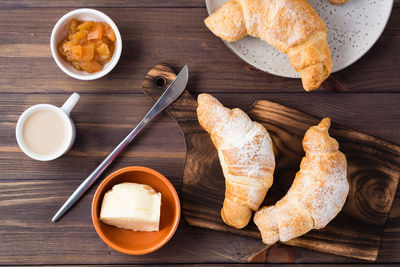 Fresh crispy croissants on a wooden board, a cup of coffee, butter and jam in bowls on the table