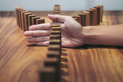 Cropped hand of person blocking wooden dominoes on table