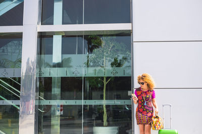 Woman using mobile phone while standing against building