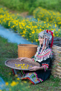 Woman in traditional clothing holding straw basket sitting at farm
